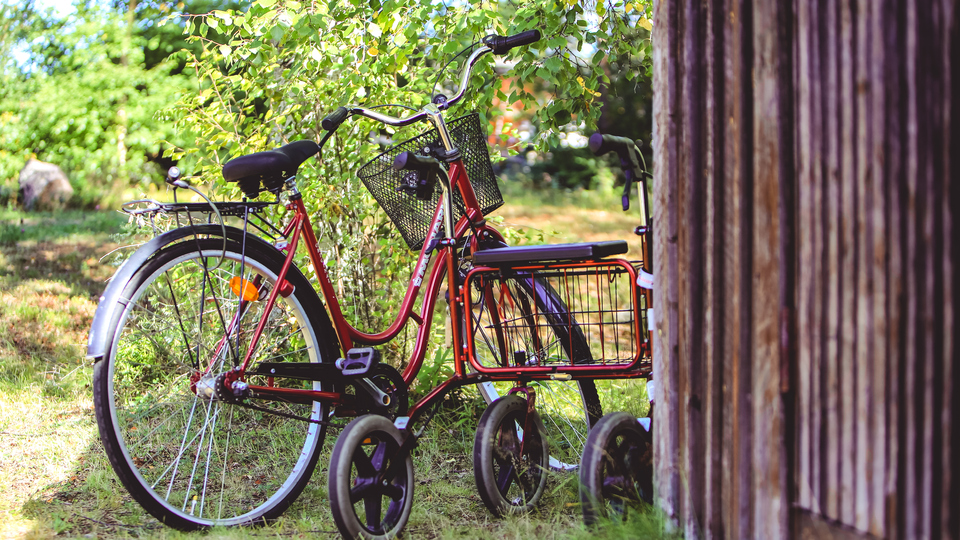Cykel och rullator  parkerade i gräset vid rödmålad husknut.