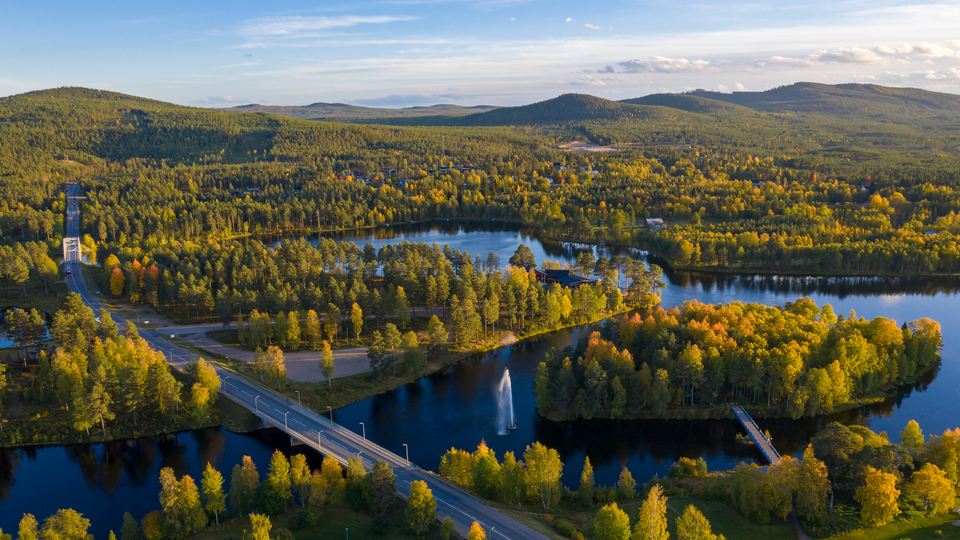 Drönarfoto över Lillön, Storön, Ljusnan och E45:an söder om Svegs centrum Sommarbild med lövträd och barrskog.