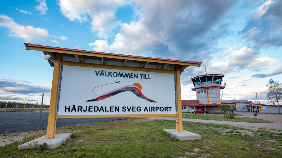 Skylt med texten Välkommen till Härjedalen Sveg airport och flygledartornet i bakgrunden.