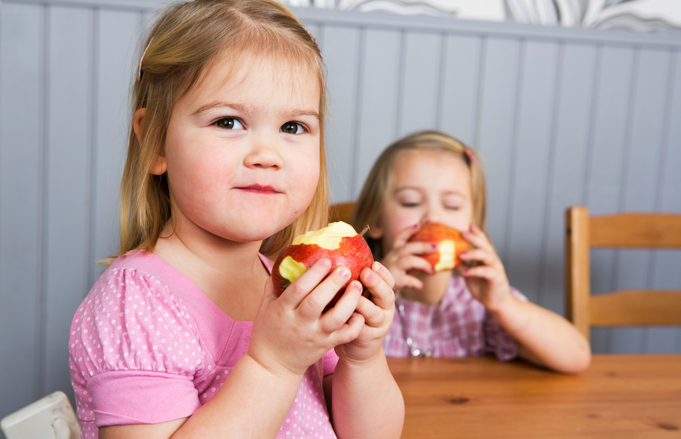 Två små flickor som äter äpple vid ett köksbord