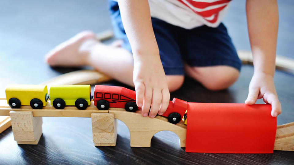 Close up photo of toddler boy playing with toy wooden train at home. Game for little children